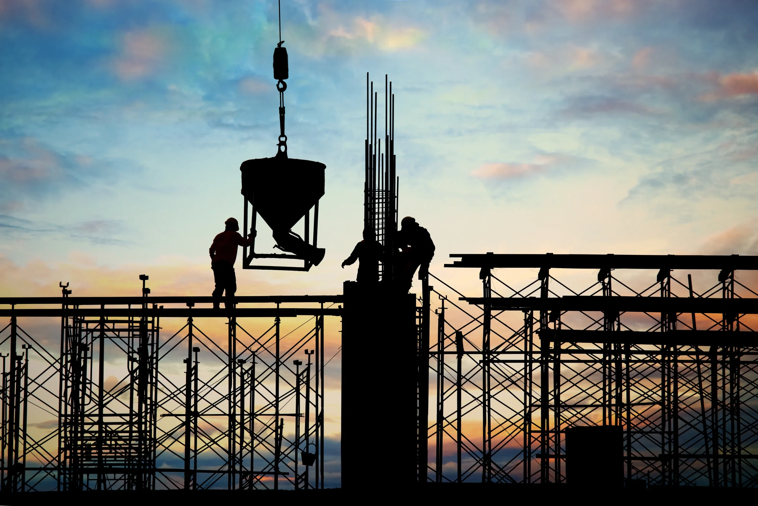Construction workers on scaffolding working at a construction site during sunset, handling materials and building structures